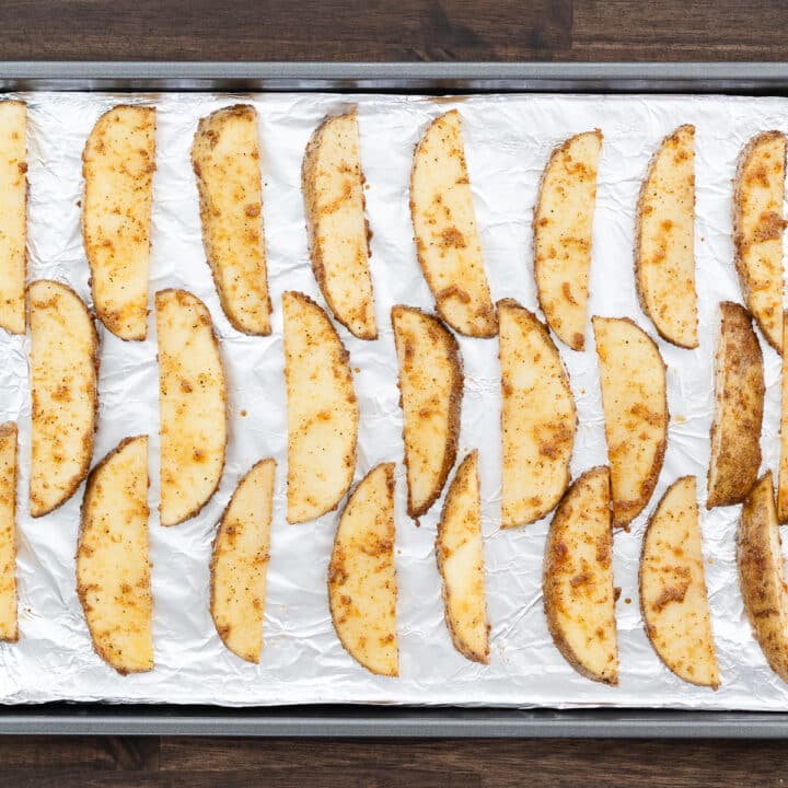 Potato wedges arranged in a single layer on a foil-lined baking tray, prepared for baking.