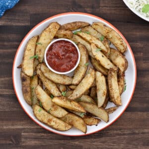 A plate of golden-brown baked potato wedges served with a side of ketchup for dipping.