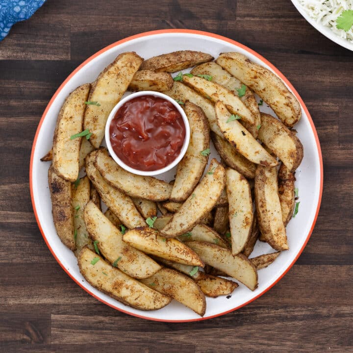 A plate of golden-brown baked potato wedges served with a side of ketchup for dipping.