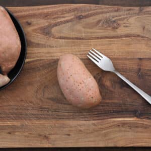 A pricked sweet potato on a wooden cutting board.