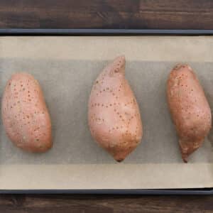 Pricked sweet potatoes arranged on a parchment-lined baking tray.