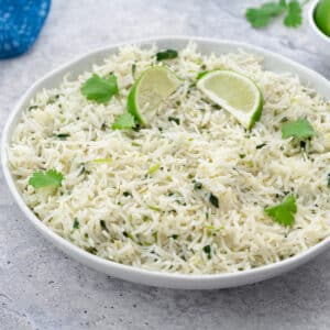 Homemade Cilantro Lime Rice in a white bowl on a white table, with cilantro leaves, and a blue towel nearby.