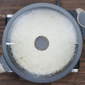 Pan with rice cooking in water, covered with a lid.