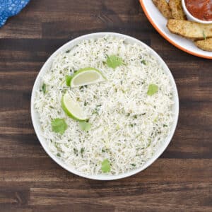 White bowl of cilantro lime rice, garnished with lime wedges and fresh cilantro.