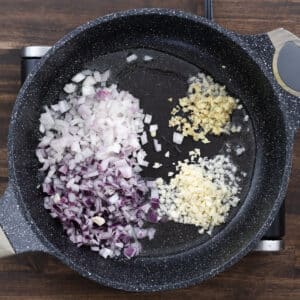 A pan filled with chopped onions, garlic, ginger, and shallots, ready for sautéing.