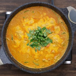 A pan of creamy coconut chicken curry garnished with freshly chopped cilantro leaves for added freshness.