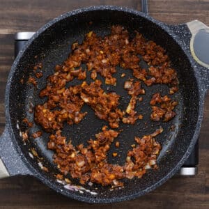 A pan of sautéed aromatics mixed with Thai red curry paste.