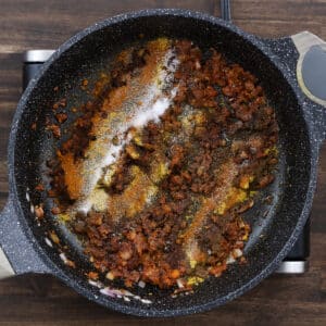 A pan with Thai red curry paste and spice powders like curry powder, paprika, and black pepper added together for sauteing.