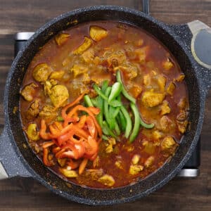 A pan with chicken in broth, along with colorful sliced bell peppers, ready to be mixed.