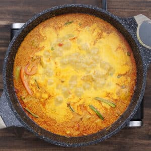 A pan of chicken in a savory coconut milk sauce, simmering and infusing flavors together.