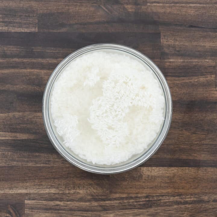 A bowl filled with uncooked rice and water, ready for rinsing.