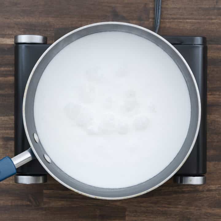 A pan showing rice simmering gently in coconut milk on the stove.