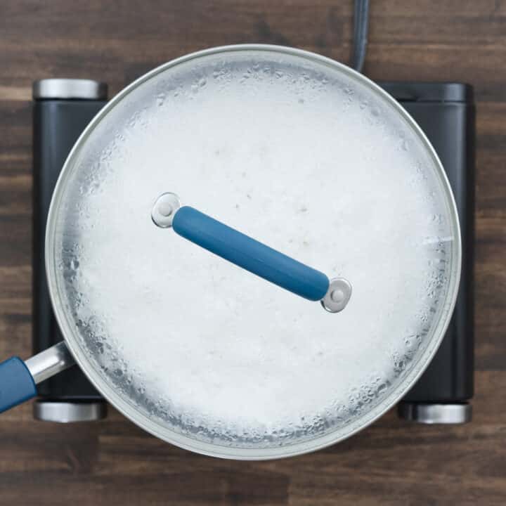 A pan with rice cooking in coconut milk, covered with a lid.