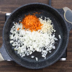 A pan on the stovetop with garlic, onions, and carrots being sautéed until aromatic.