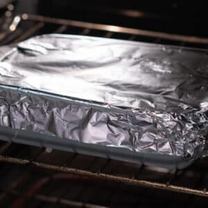 A baking dish covered with aluminum foil, placed inside a preheated oven.