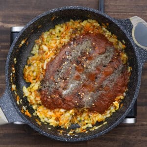 A pan with sautéed aromatics, crushed tomatoes, and seasonings added for flavor.