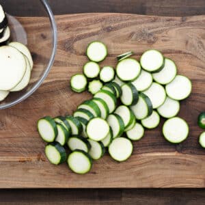 A cutting board with zucchini sliced into even, circular pieces.