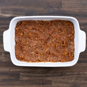 A baking dish with an even layer of tomato sauce spread across the bottom.