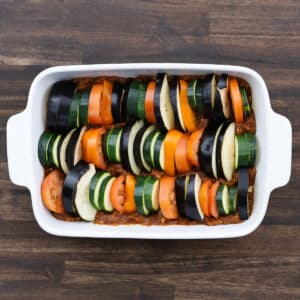 A baking dish with layers of tomato sauce and arranged sliced veggies on top.