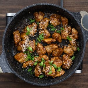 A pan with sesame chicken garnished with sesame seeds and spring onions.