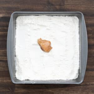 A tray with the flour mixture and marinated chicken.