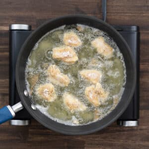 A pan with flour-coated chicken frying in oil.