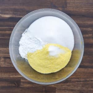 The dry ingredients, such as cornmeal, flour, sugar, baking powder, and salt, in a mixing bowl.