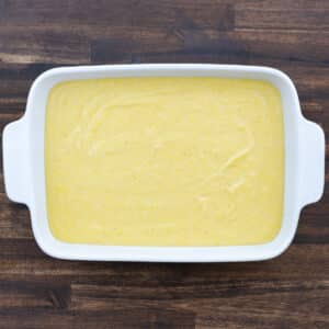 The prepared cornbread batter is poured into a greased baking dish, spread evenly to prepare for baking.