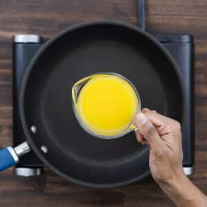 A close-up of a jug filled with orange juice, ready to be poured into a cooking pan for cranberry sauce.