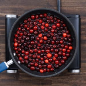 Fresh cranberries in a pan, coated with the orange juice and sugar mixture, ready to be cooked.