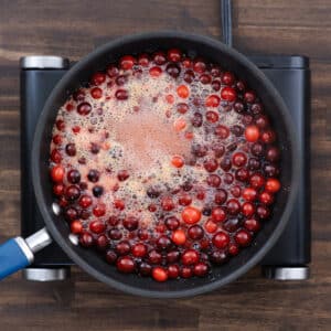 Cranberries gently simmering in a pan, starting to soften as they cook in the sweet orange syrup.