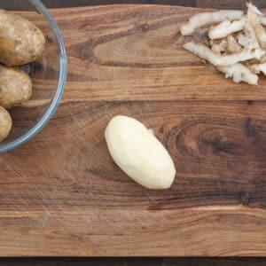 A cutting board with peeled potatoes ready for cutting.