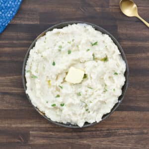 Mashed potatoes served with a pat of butter and garnished with cilantro leaves.