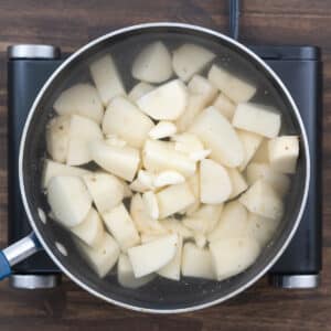 A pot filled with potatoes and water, along with crushed garlic.