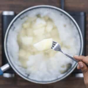 Showing the fork easily piercing through soft potatoes, confirming they are cooked to perfection.