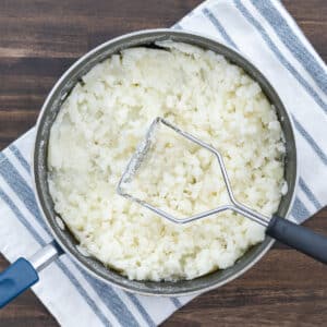 A pot with partially mashed potatoes and a masher.