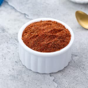 Homemade pork chop dry rub seasoning in a small white bowl on a white table, with a golden spoon beside it.