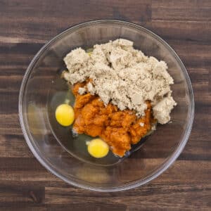 A mixing bowl containing pumpkin puree, eggs, and brown sugar, ready to be combined for the pumpkin pie filling.