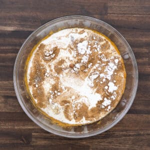 A bowl holding pumpkin puree, fall spices, and milk, ready to be mixed for the pie filling.