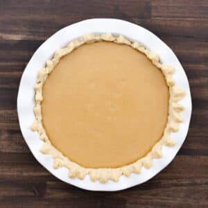A pie crust filled with creamy pumpkin pie filling, ready to be baked.
