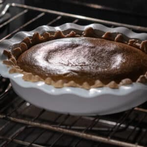 A fully baked pumpkin pie inside the oven, golden and slightly jiggly at the center.