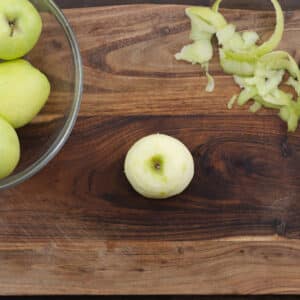 A cutting board with peeled green apples.