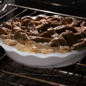 A nearly baked apple pie in the oven, its lattice crust golden and crisp.