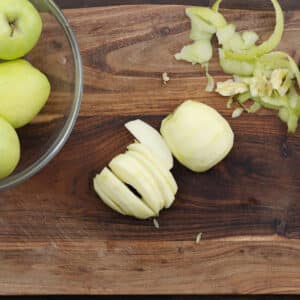 A cutting board with peeled and sliced green apples.