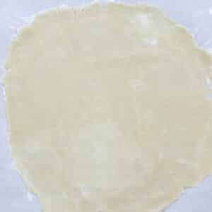 A smooth, round sheet of pie dough rolled out on parchment paper, ready for use.