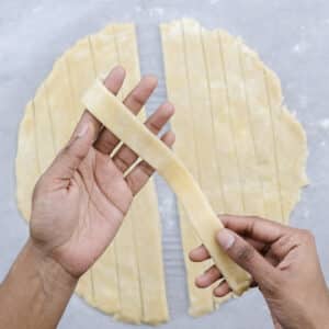 Evenly cut strips of rolled pie dough arranged on parchment paper for the lattice crust.