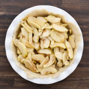 A pie dish filled with seasoned apple slices placed on top of the bottom crust.