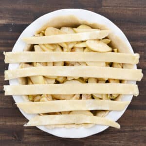 Apple pie filling topped with parallel strips of dough in preparation for a lattice design.