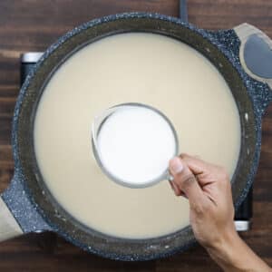 A pan with the roux and chicken broth mixture, with milk about to be added for creamy texture.