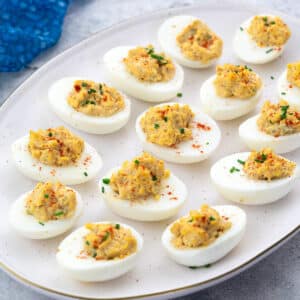 Homemade deviled eggs on an oval plate, set on a white table with a blue towel.